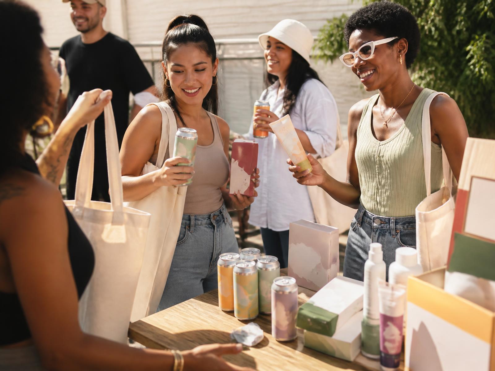 People receiving colorful canned beverages, skincare, snacks and tote bags at a sunny community event